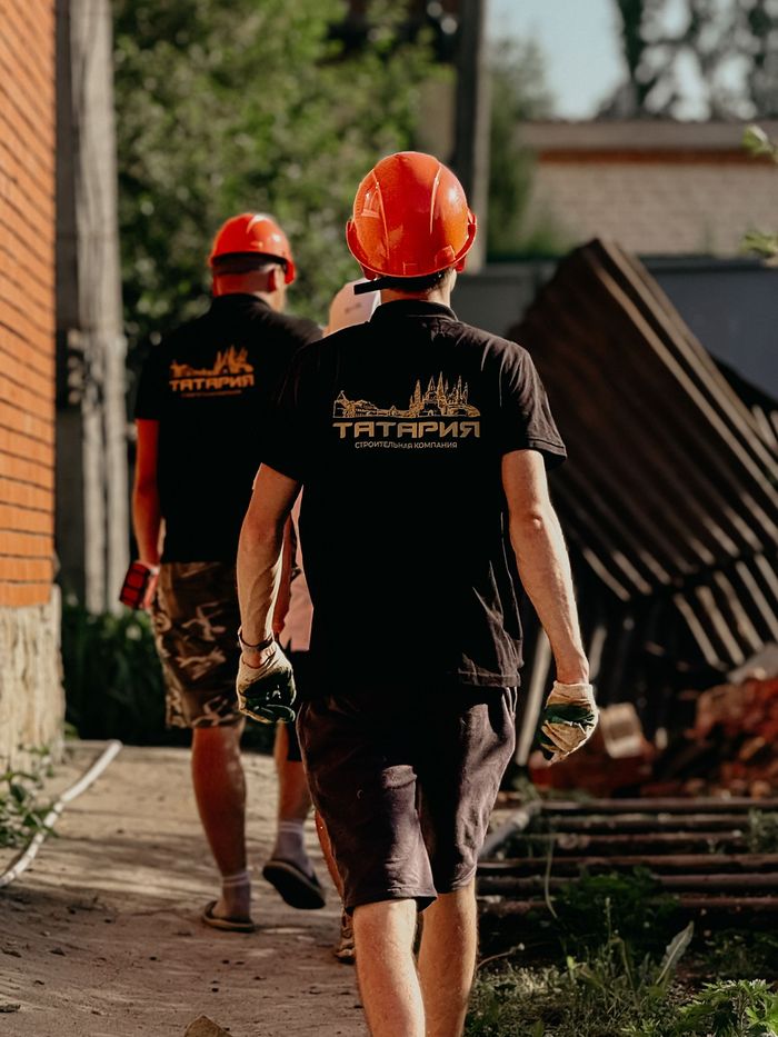 Dois trabalhadores de capacete caminhando por um canteiro de obras no fim da tarde.